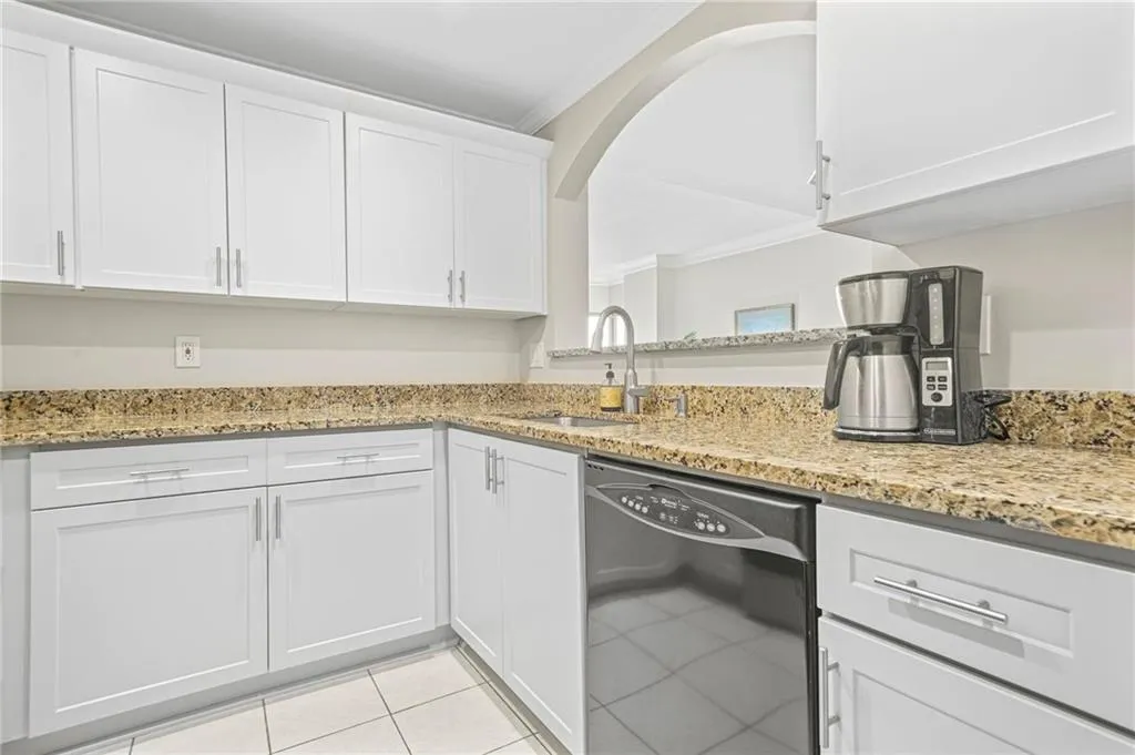 Kitchen with black dishwasher, crown molding, a sink, light tile patterned floors, and white cabinetry