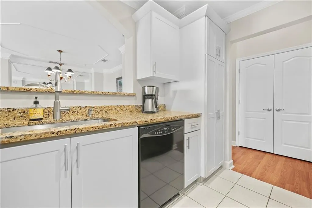Kitchen featuring black dishwasher, ornamental molding, a sink, light tile patterned flooring, and white cabinetry