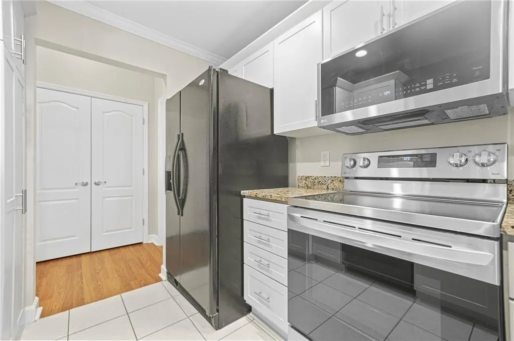 Kitchen featuring stainless steel appliances, ornamental molding, white cabinetry, light tile patterned floors, and light stone counters