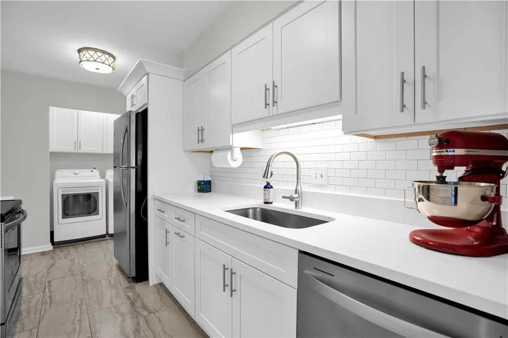 Kitchen with washer / clothes dryer, stainless steel appliances, white cabinets, light stone counters, and backsplash