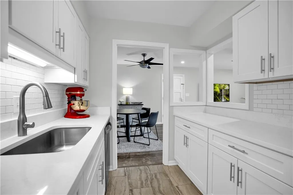 Kitchen featuring backsplash, white cabinets, light stone countertops, and ceiling fan