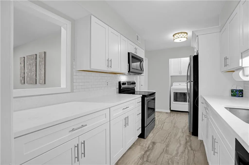 Kitchen with stainless steel appliances, white cabinetry, washer / dryer, and light stone countertops