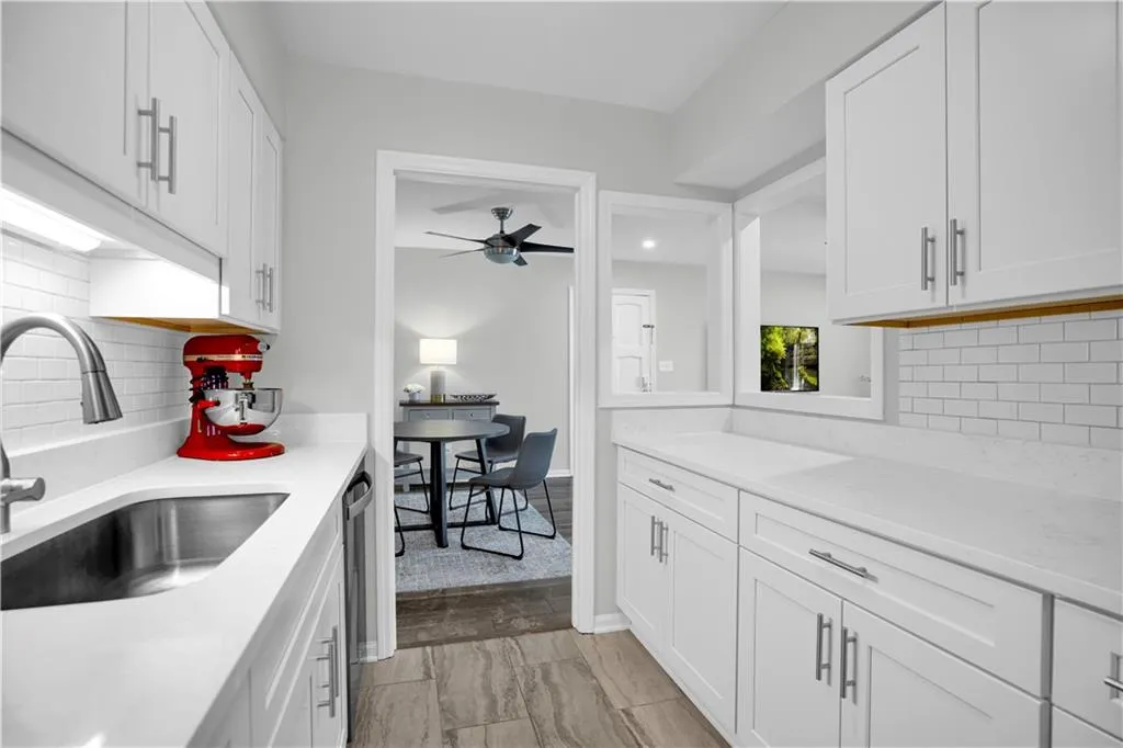 Kitchen with backsplash, white cabinets, light stone countertops, and a ceiling fan