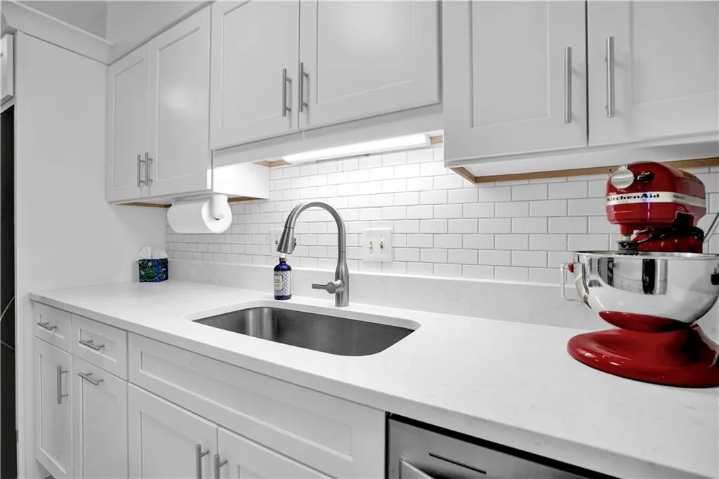 Kitchen featuring light stone counters, white cabinets, and backsplash