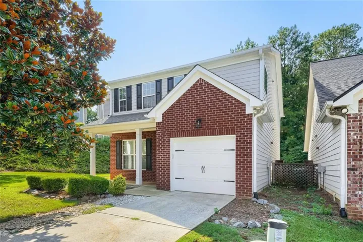 Brick and siding exterior featuring a covered front entry, attached garage, and upper-level windows with shutters