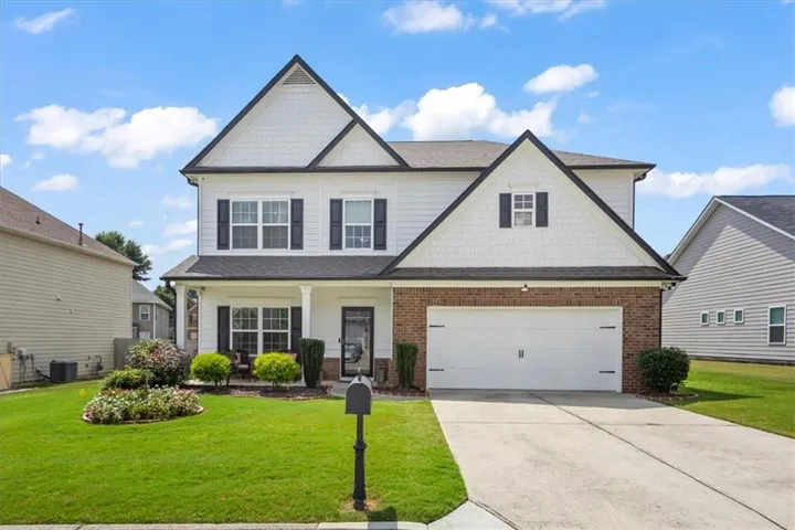 Two-story residence featuring a brick and siding exterior, a two-car garage, and a covered front porch