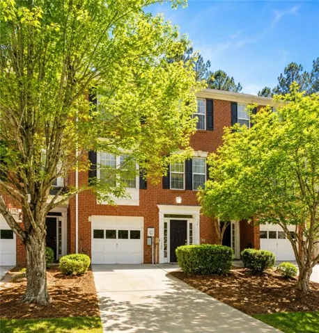 Brick townhome exterior featuring black shutters, a white framed entry, and an integrated garage with a panel door