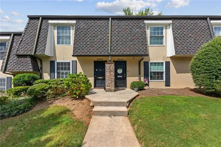Townhome exterior featuring a dormer roof, stone facade accents, and a paved walkway