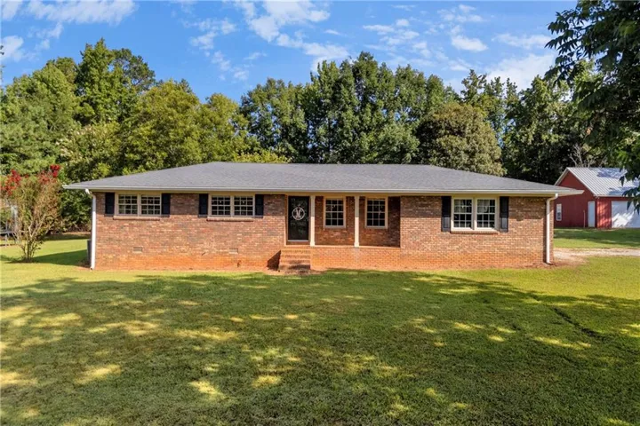Brick exterior with white window frames and dark shutters, featuring a covered entry and a gray shingle roof