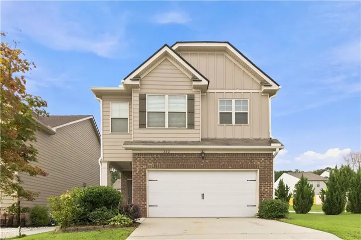 Two-story residence featuring a brick and siding exterior, an attached garage, a paved driveway, and mature landscaping