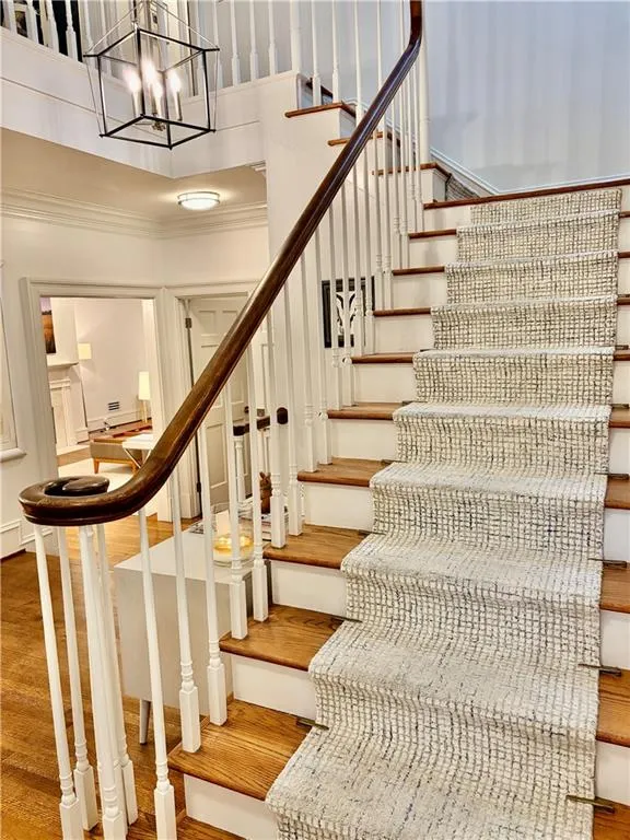 Hardwood staircase with white balusters, wood-finish handrail, and lantern-style chandelier