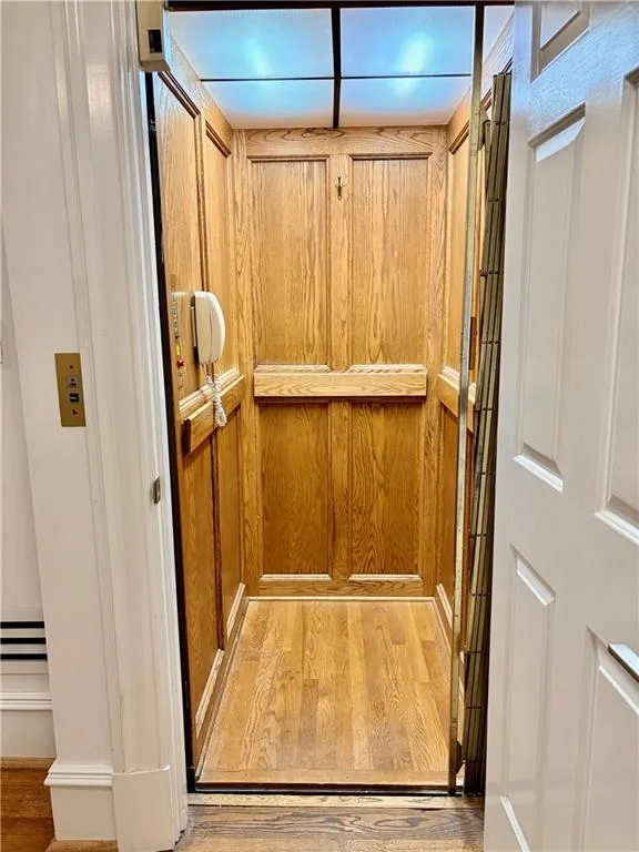 Interior elevator featuring wood paneling, wood-finish flooring, a built-in bench, and an integrated ceiling light fixture