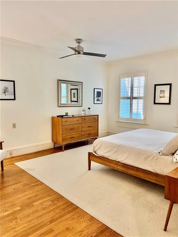 Hardwood flooring, crown molding, ceiling fan, window with interior shutters, and neutral wall tones