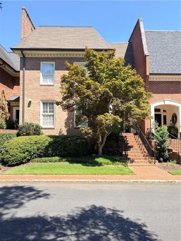 Brick exterior with a gabled roofline, featuring brick steps with iron railings, and mature landscaping