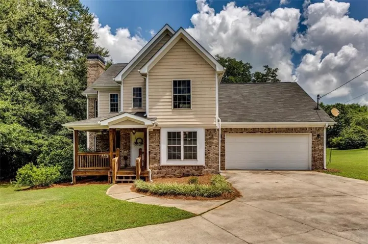 Two-story residence featuring a combination of brick and siding, an attached two-car garage, a covered front porch with wooden railings, a concrete driveway, and a well-maintained lawn