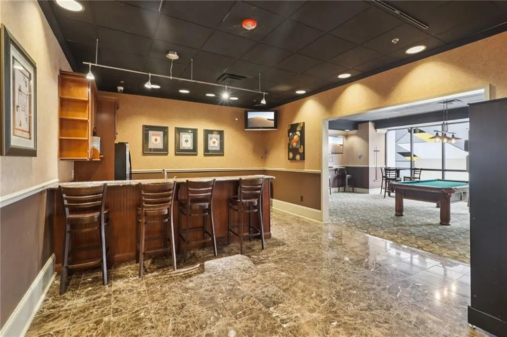 Indoor dry bar featuring fridge, billiards table, wainscoting, granite floors, and baseboards