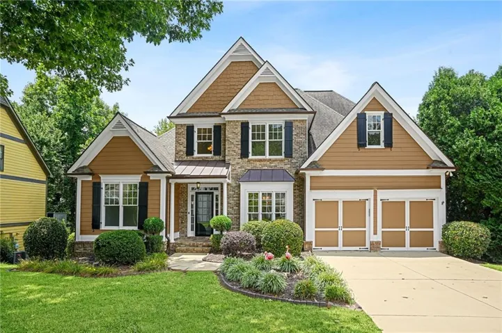 Two-story residence featuring a stone and siding facade, a two-car garage, and a manicured front lawn