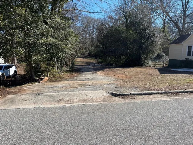 Property features a clear drive entrance with an unpaved surface, bordered by established trees and natural foliage