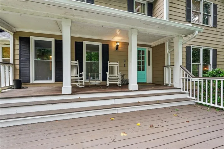 Wrap-around porch featuring white columns and railing, a turquoise front door, and a wall-mounted light fixture