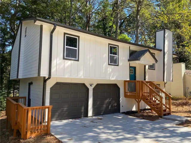 Split-level exterior featuring white siding, dark trim windows, a covered entry with a vibrant blue door, a wood-finish staircase, and an attached two-car garage