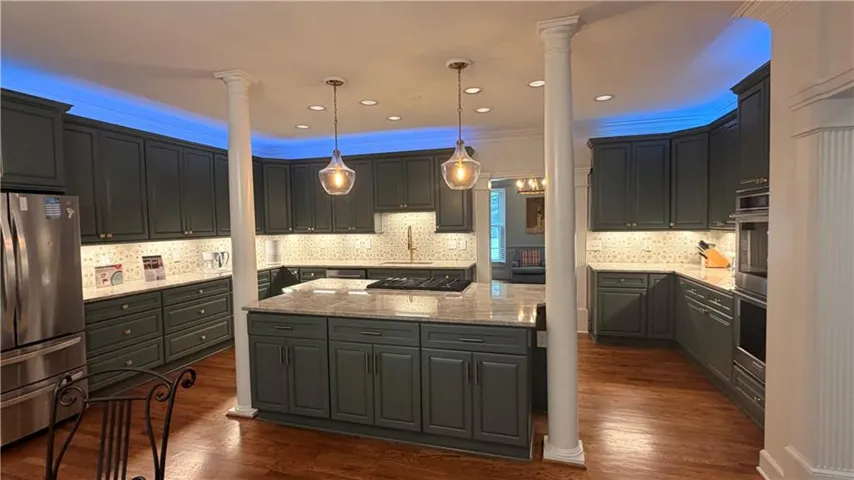 Kitchen with dark cabinetry, integrated stainless steel appliances, recessed lighting, and an island with a built-in cooktop
