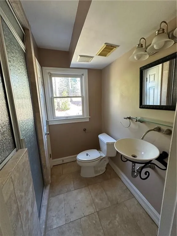 Bathroom featuring toilet, baseboards, visible vents, and a stall shower