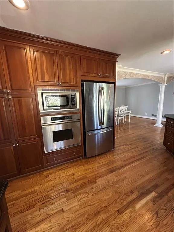 Kitchen with oven, ornamental molding, freestanding refrigerator, arched walkways, and ornate columns