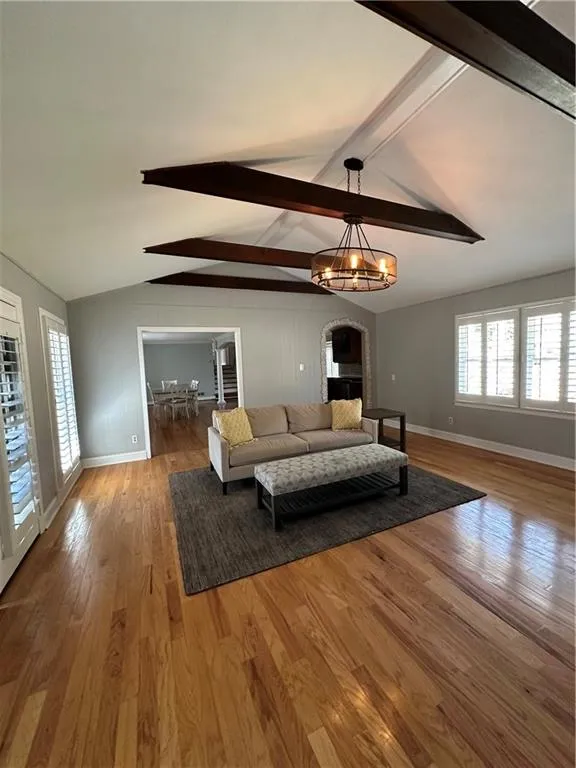 Living room with a notable chandelier, vaulted ceiling with beams, wood finished floors, and baseboards