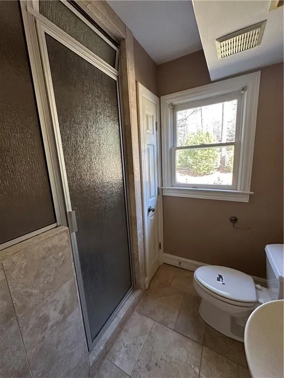 Full bathroom featuring visible vents, toilet, a shower stall, tile patterned flooring, and baseboards