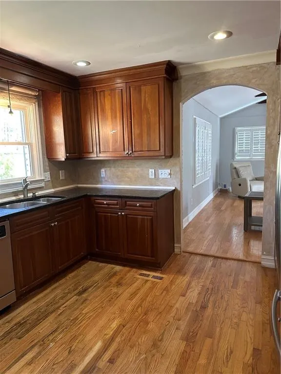 Kitchen with dishwashing machine, wood finished floors, arched walkways, a sink, and dark countertops