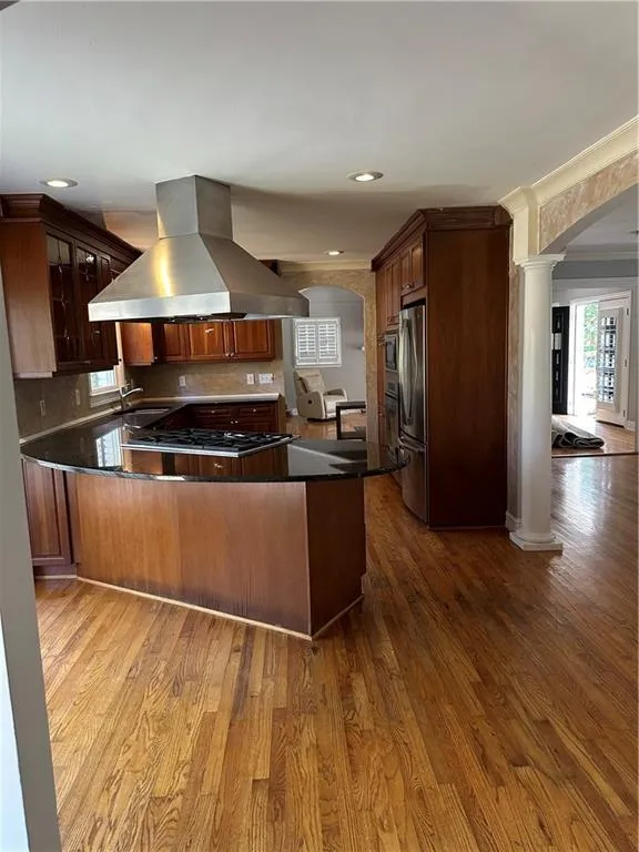 Kitchen with dark wood-style floors, ventilation hood, arched walkways, cooktop, and ornate columns