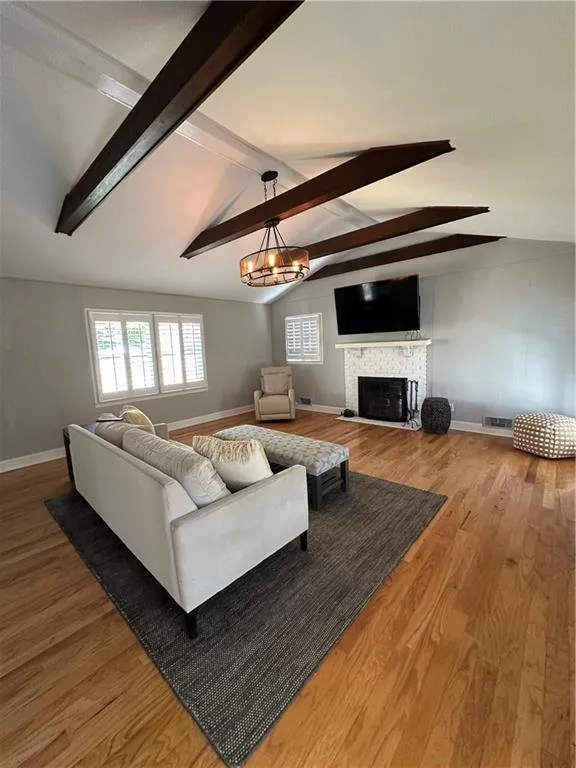 Living area featuring light wood finished floors, visible vents, a fireplace with raised hearth, baseboards, and lofted ceiling with beams