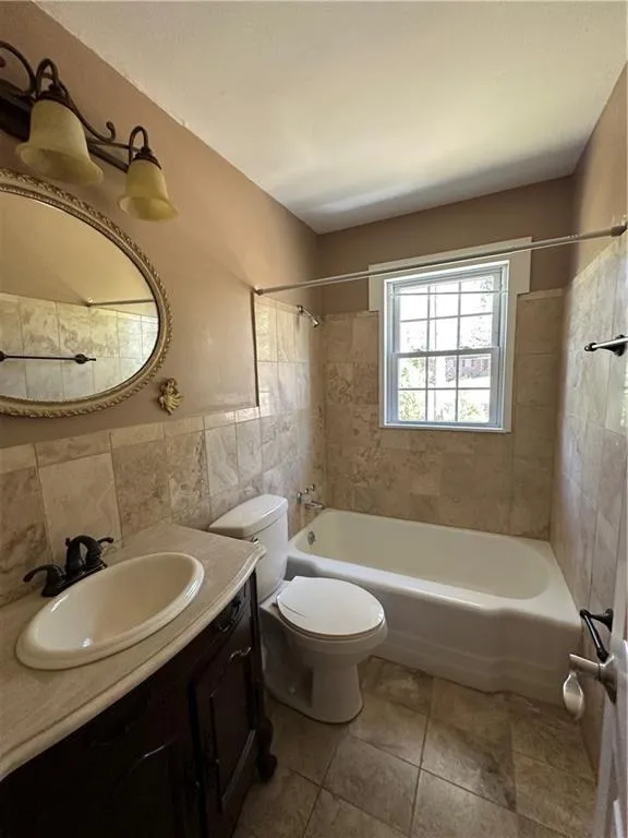 Bathroom featuring vanity, toilet, tile patterned flooring, tile walls, and bathing tub / shower combination