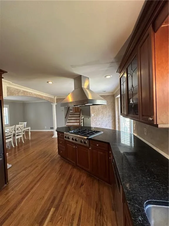 Kitchen with glass insert cabinets, baseboards, dark wood-type flooring, wall chimney range hood, and stovetop