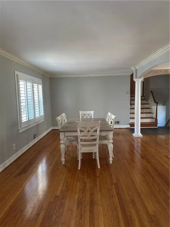 Unfurnished dining area featuring wood finished floors, arched walkways, and ornamental molding