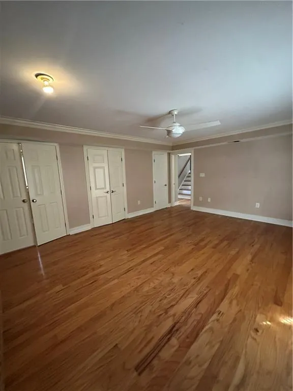 Unfurnished living room featuring stairway, a ceiling fan, wood finished floors, baseboards, and crown molding