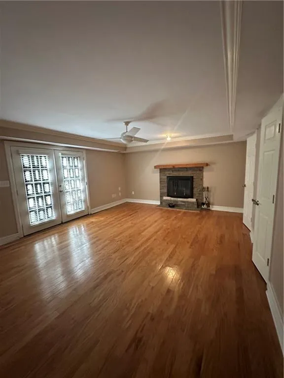 Unfurnished living room featuring wood finished floors, a brick fireplace, a ceiling fan, and baseboards