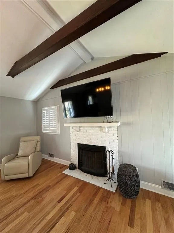 Living room with visible vents, a fireplace, lofted ceiling with beams, and wood finished floors