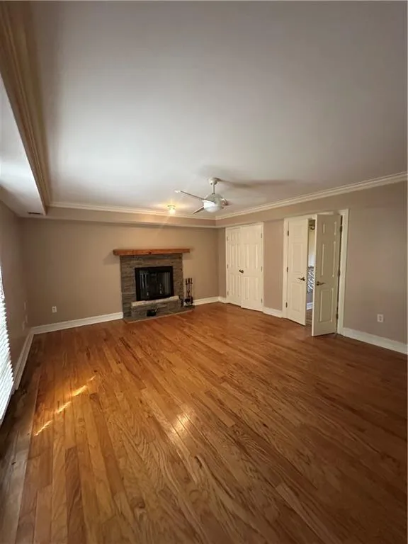 Unfurnished living room featuring wood finished floors, a ceiling fan, baseboards, and a fireplace with raised hearth
