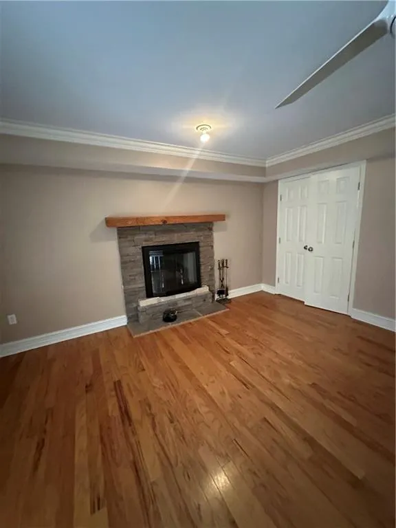 Unfurnished living room with baseboards, wood finished floors, a fireplace, and ornamental molding
