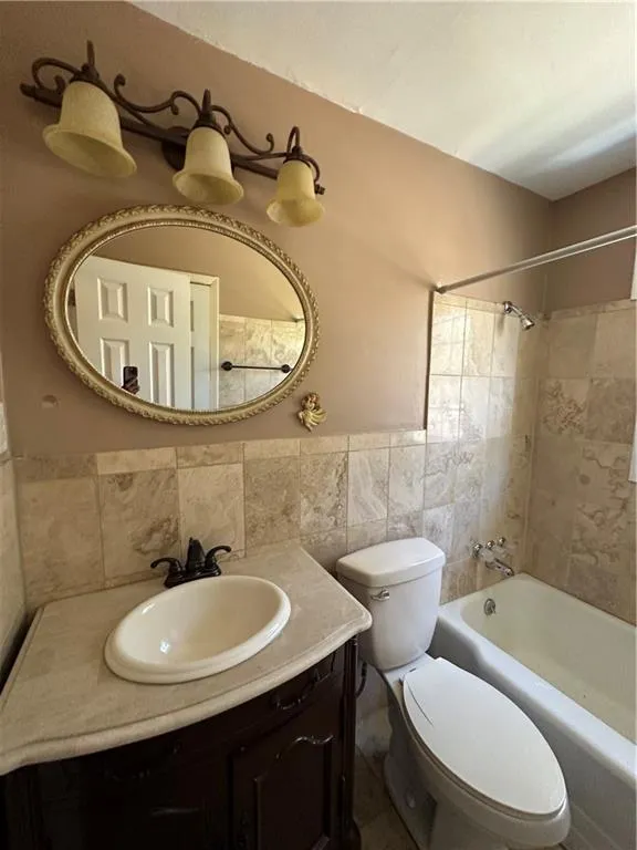 Bathroom with vanity,  shower combination, wainscoting, tile walls, and toilet