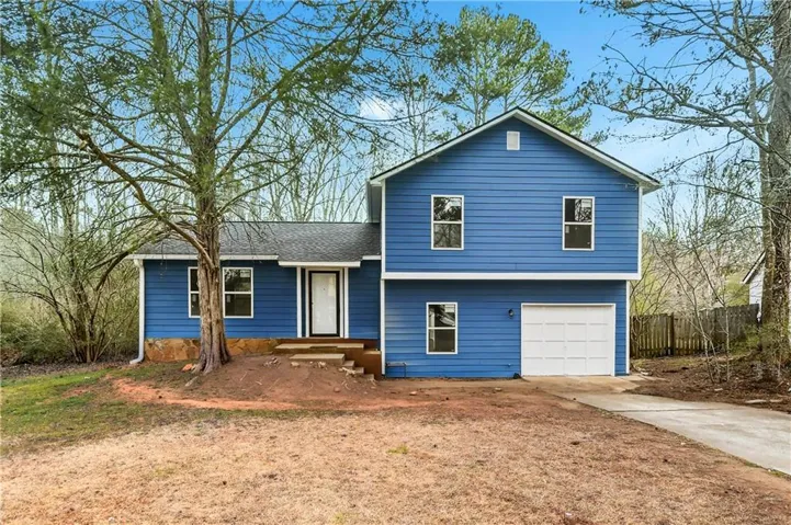 Split level home with a garage, concrete driveway, and roof with shingles