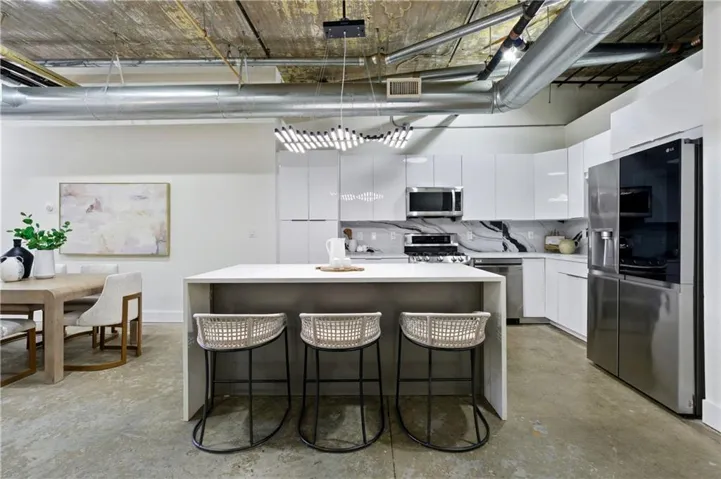 Kitchen featuring a kitchen bar, stainless steel appliances, a center island, modern cabinets, and concrete flooring