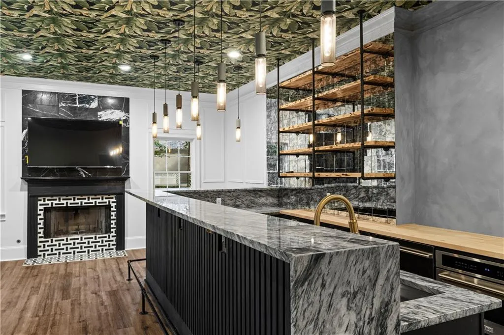 Bar area with pendant lighting, ornamental molding, a tiled fireplace, wood finished floors, and dark cabinets