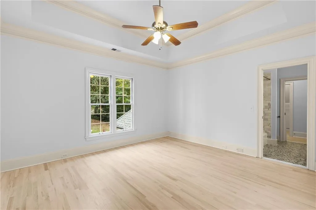 Unfurnished room featuring a tray ceiling, light wood-type flooring, a ceiling fan, and crown molding