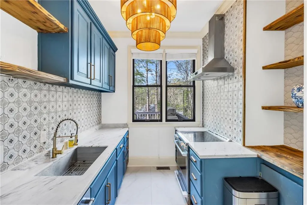 Kitchen with open shelves, tasteful backsplash, blue cabinetry, and wall chimney exhaust hood