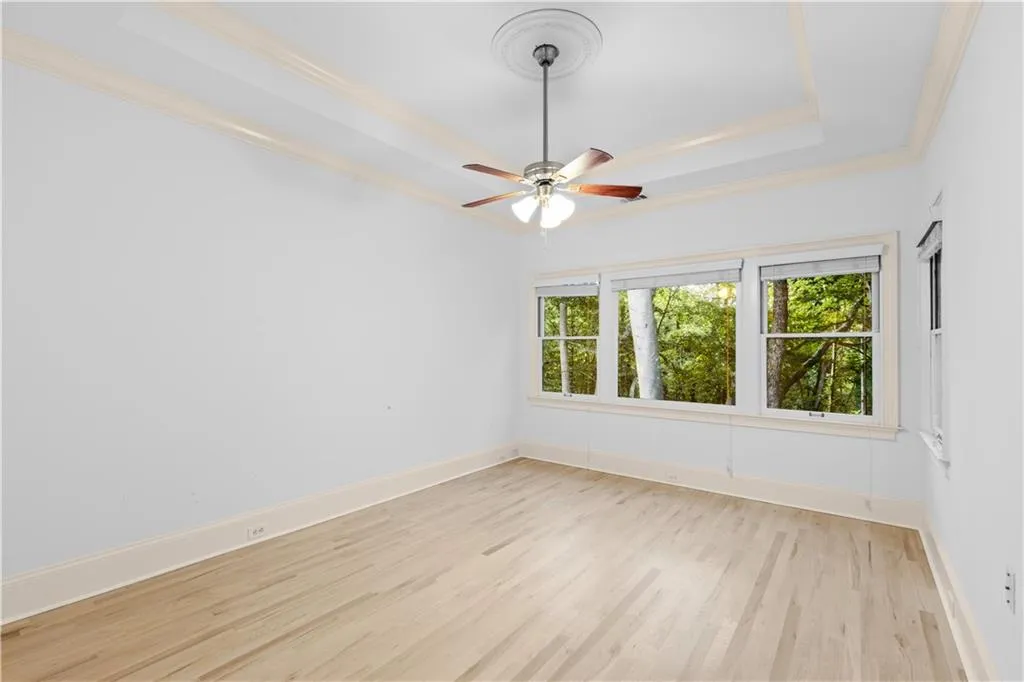 Unfurnished room featuring a tray ceiling, light wood-style floors, ornamental molding, and ceiling fan