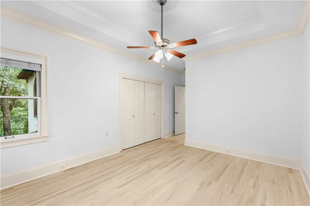 Unfurnished bedroom with wood finished floors, ornamental molding, a ceiling fan, a closet, and a raised ceiling
