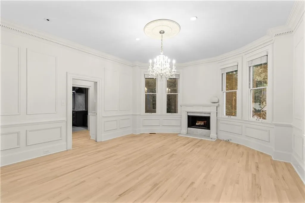 Unfurnished living room featuring a fireplace, a chandelier, light wood-style flooring, crown molding, and a decorative wall