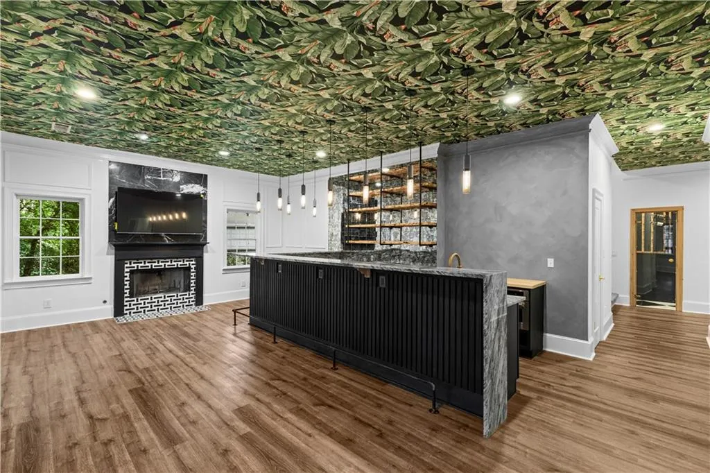 Bar featuring dark cabinets, hanging light fixtures, wood finished floors, plenty of natural light, and ornamental molding